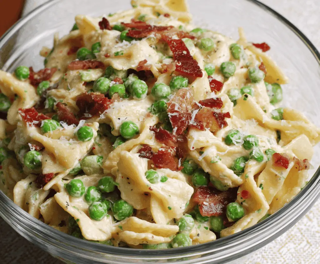 Creamy pea and bacon pasta salad in a bowl topped with fresh herbs, perfect for a refreshing summer side dish.