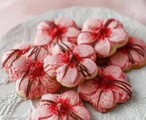 Delicious Sweet Cherry Blossom Cookies with pink icing and blossom-shaped decorations on a white plate.