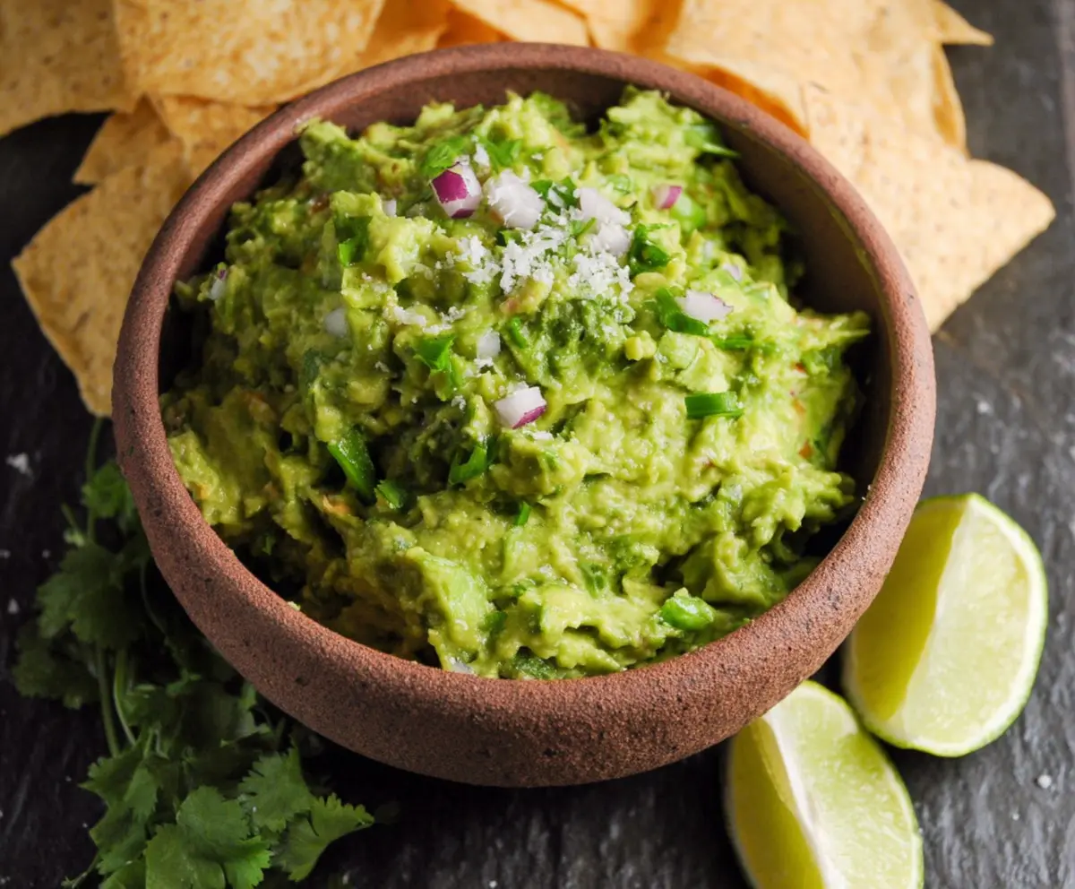 Creamy homemade guacamole with ripe avocados, tomatoes, onions, and cilantro served in a bowl.